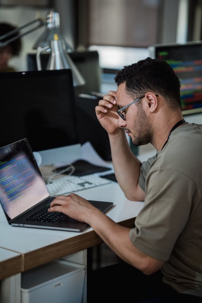A man intensely focused on coding at a desk in a modern office environment.