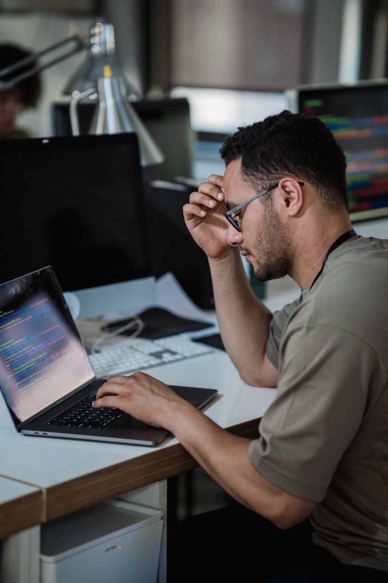 A man intensely focused on coding at a desk in a modern office environment.