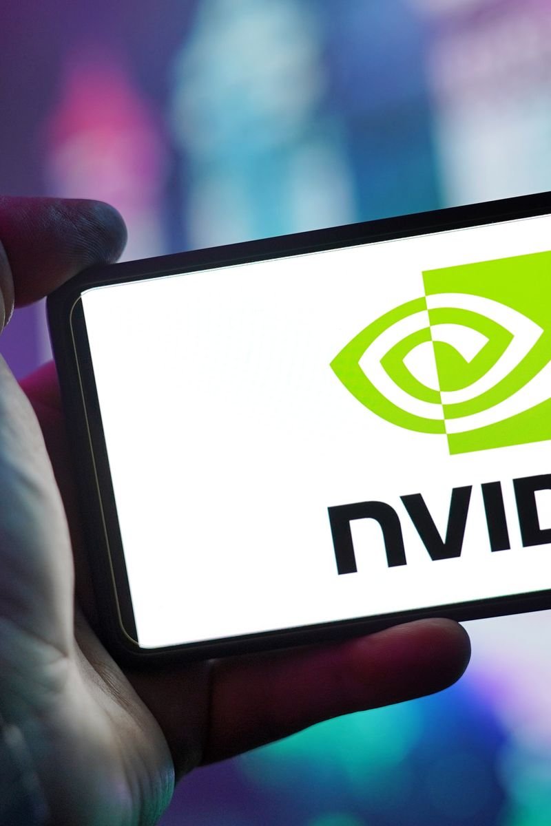 Close-up of a hand holding a smartphone showing the NVIDIA logo on screen with a blurred background.