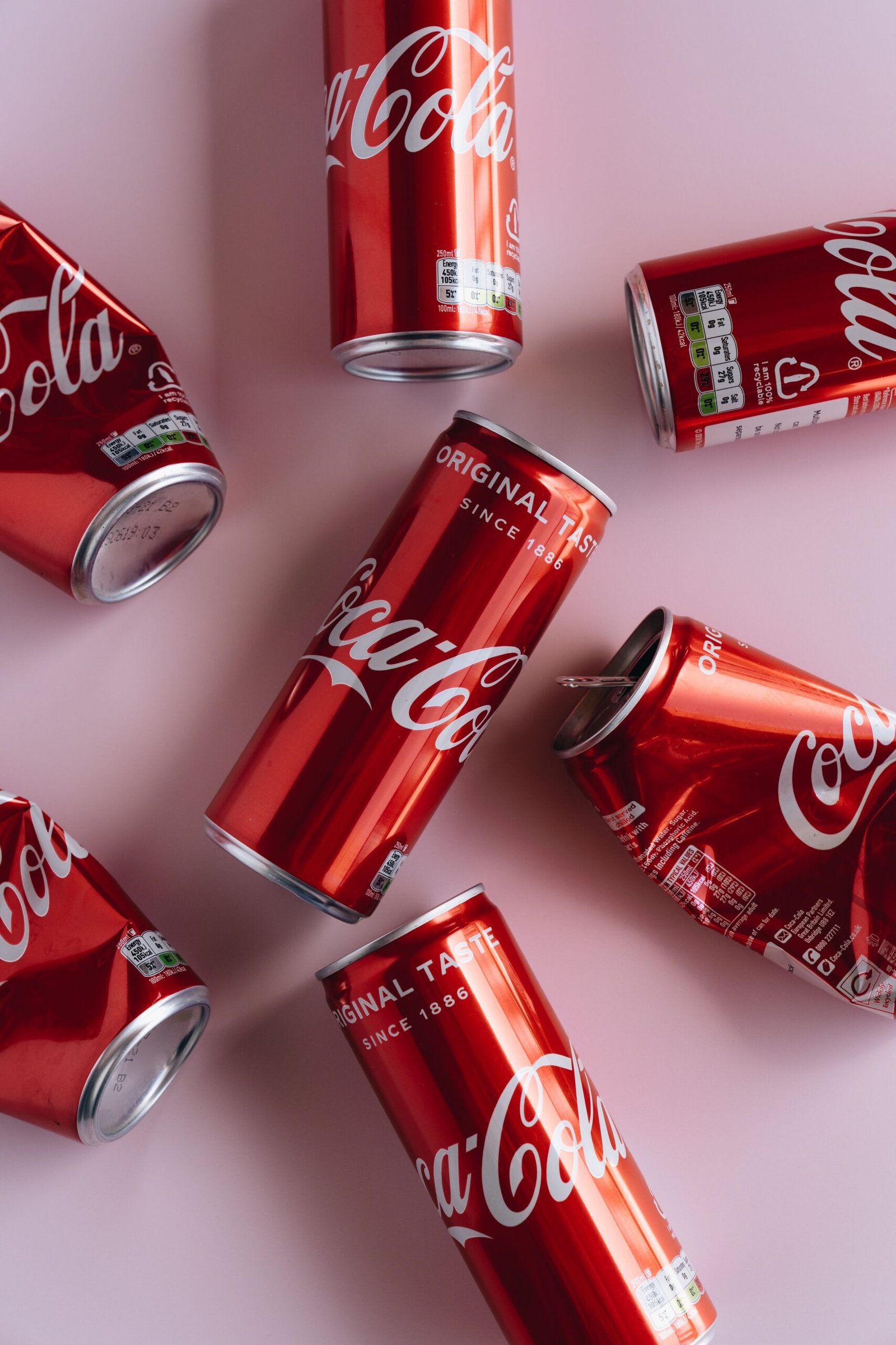 Top view of several Coca-Cola cans scattered on a light pink background.