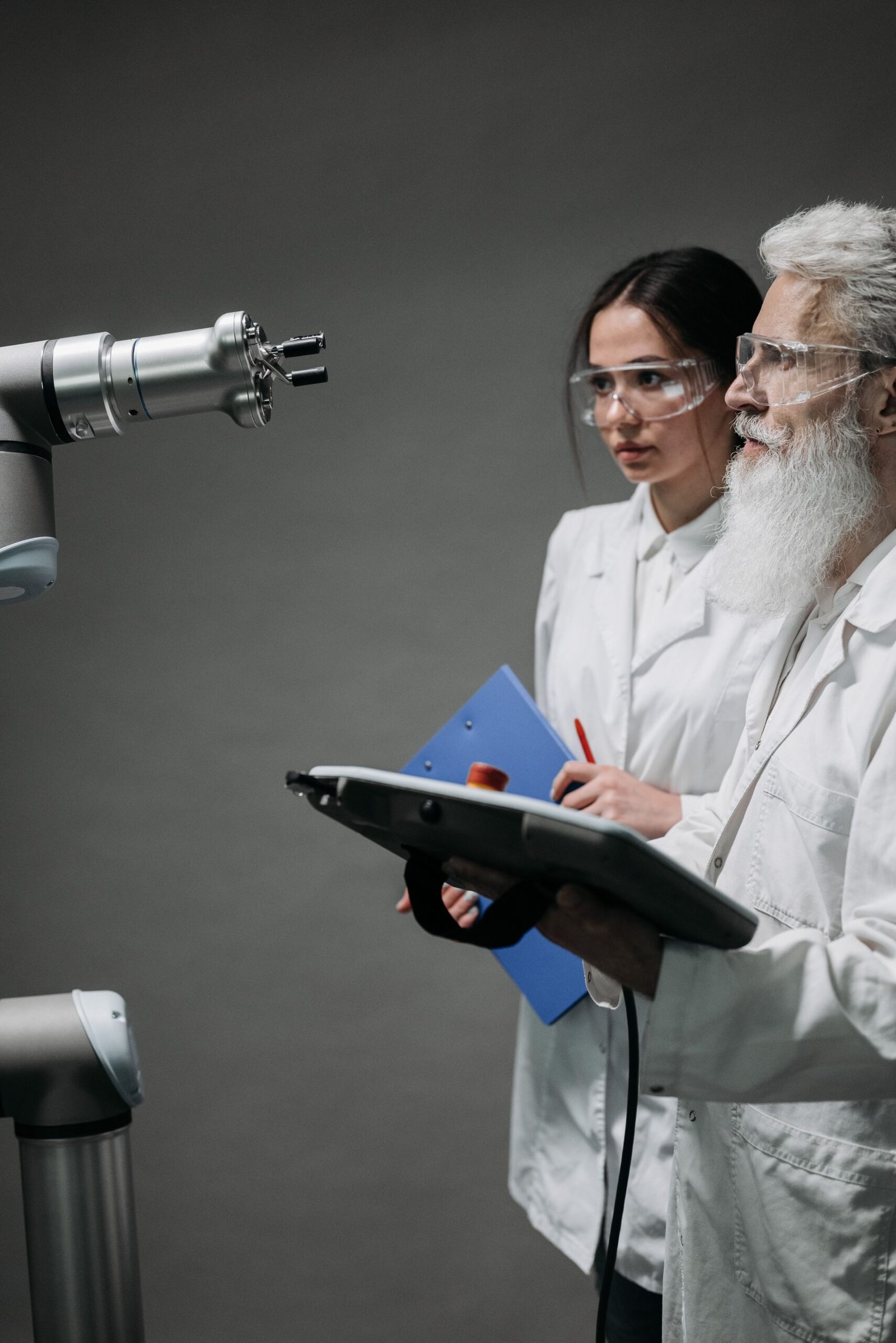 Two scientists in lab coats examine a robotic arm during a studio shoot.